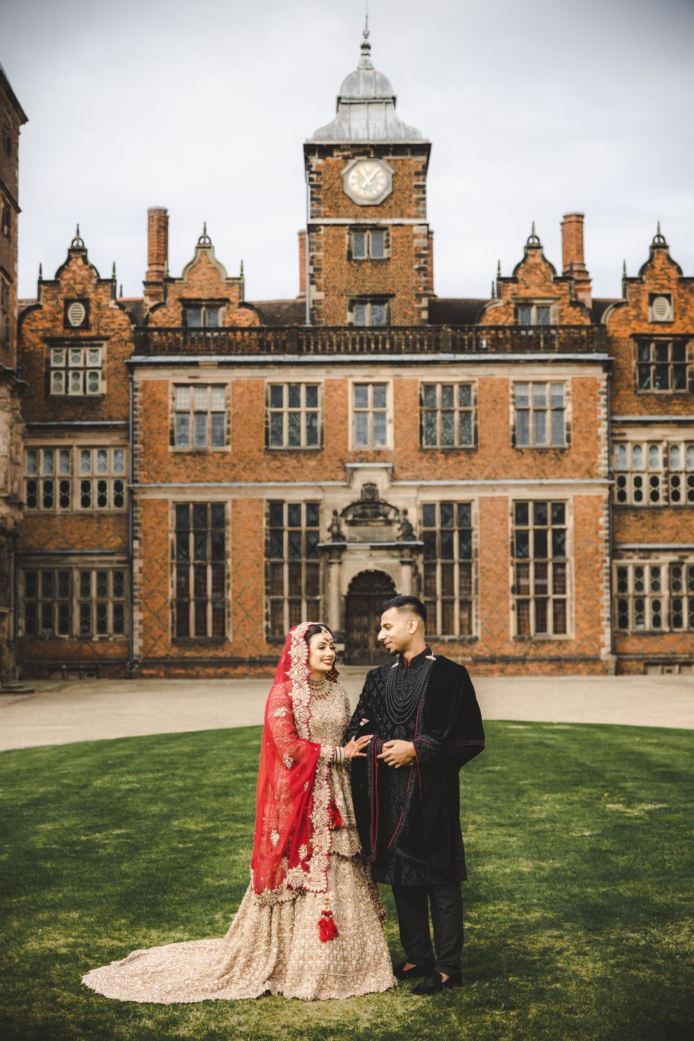 South Asian wedding couple in traditional attire photographed before historic clock tower building.