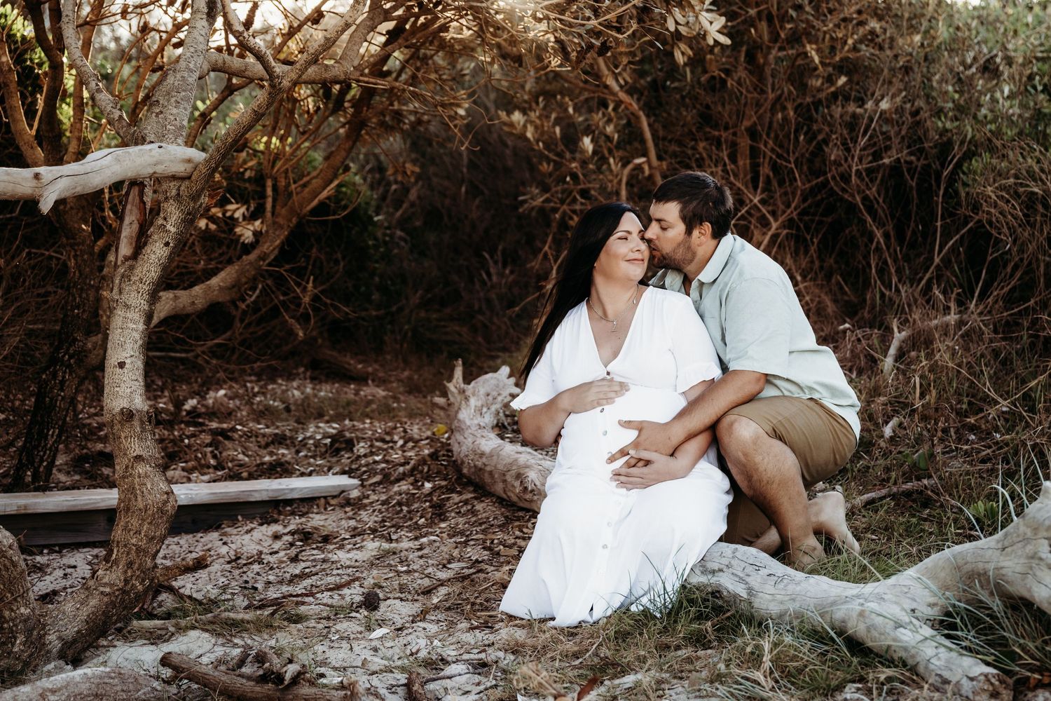 A romantic couple sharing an intimate moment on a fallen tree in a natural setting.