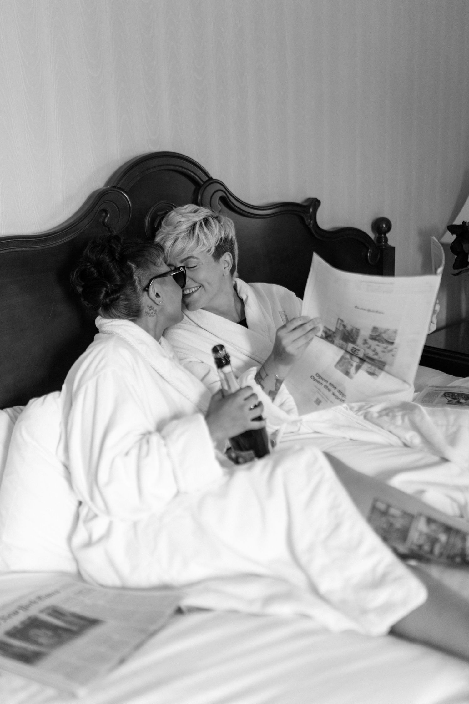 A black and white photo of two people in bathrobes reading newspapers together in bed.