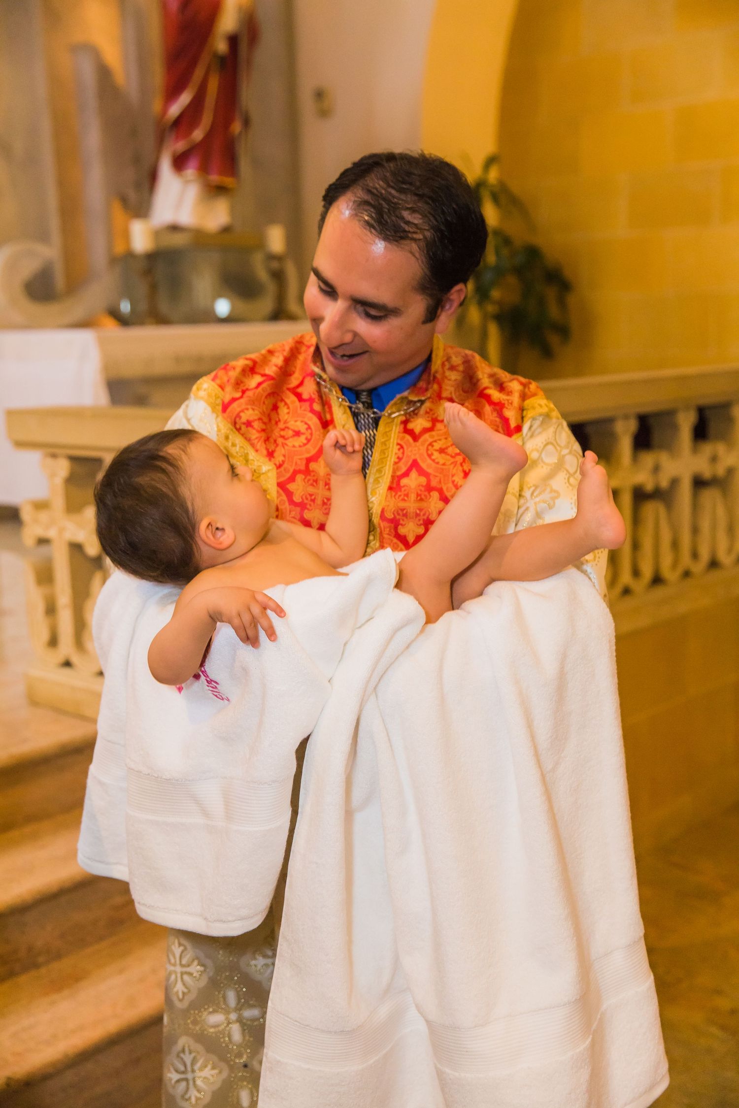 Tender embrace between parent in orange vestment and child in white during religious ceremony.