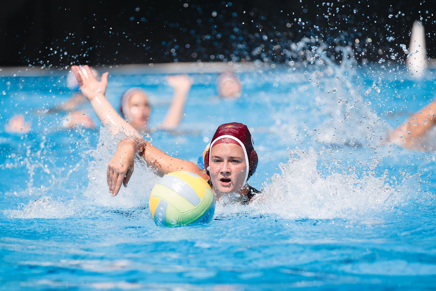 Water polo player in red cap handling ball during intense match action.