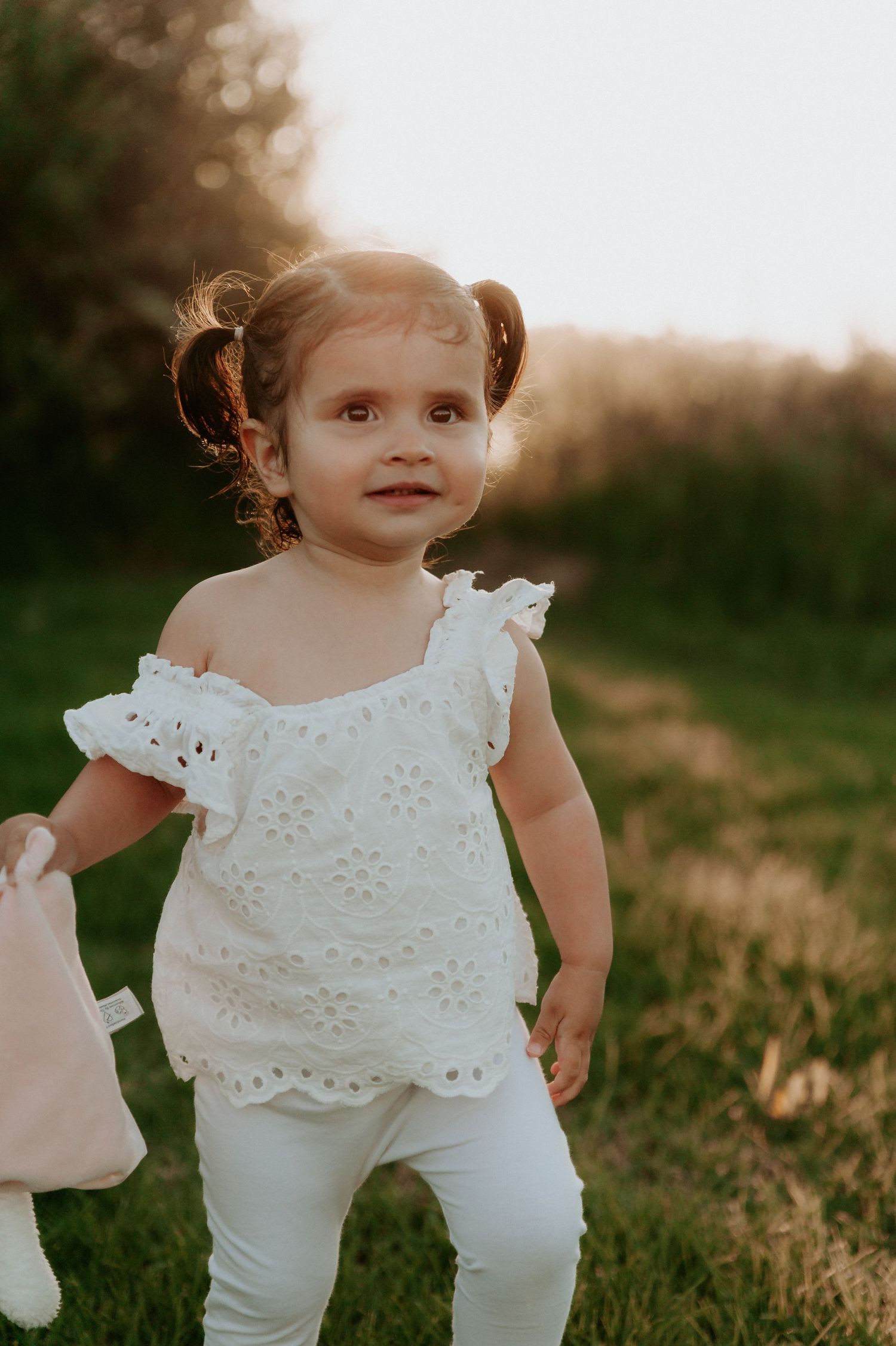 A toddler in an eyelet lace white dress plays outdoors at sunset in a grassy field.
Altona Family Photographer Melbourne