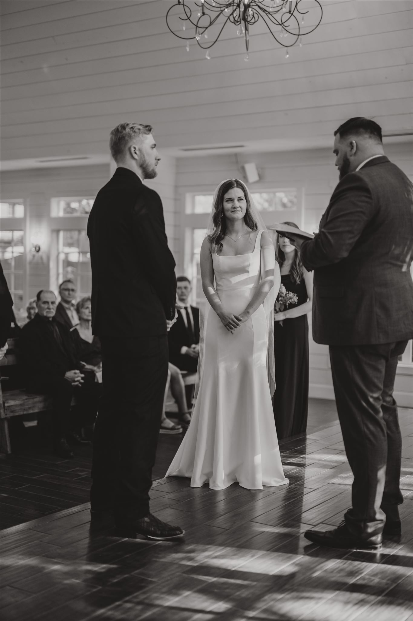 Wedding ceremony taking place in an elegant indoor venue with chandelier lighting and guests in attendance.