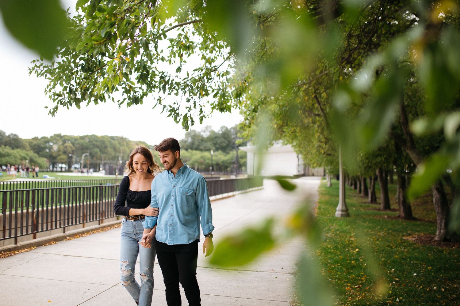 woman wearing denim and black and man wearing button down shirt and jeans walk hand in hand during their photo shoot