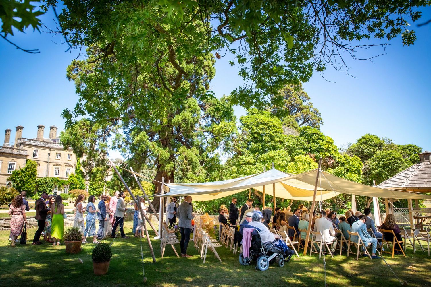 Wedding guests enjoy an outdoor garden reception under trees with string lights and white tents.