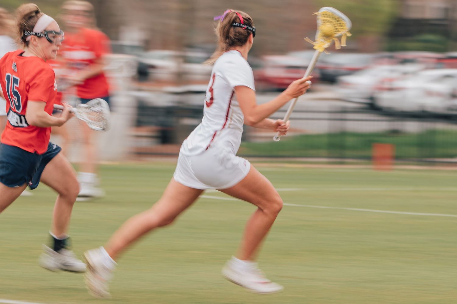 Lacrosse players in motion during a competitive match on an outdoor field.