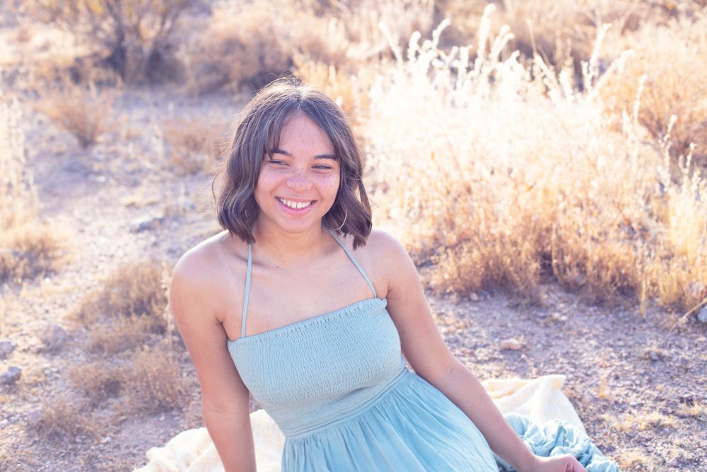 Woman in pale blue dress smiles brightly in desert landscape.