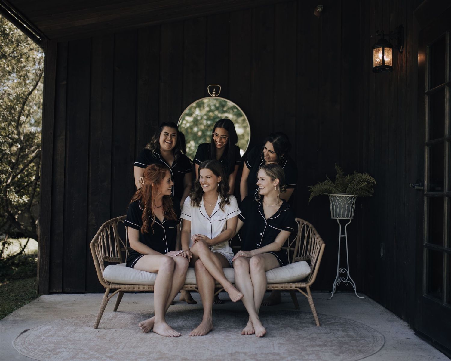 Group posed together on outdoor patio bench against black wall with circular mirror.