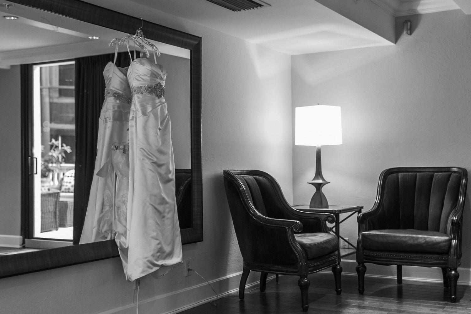 A white wedding dress hangs in a room with elegant furniture and soft lighting.