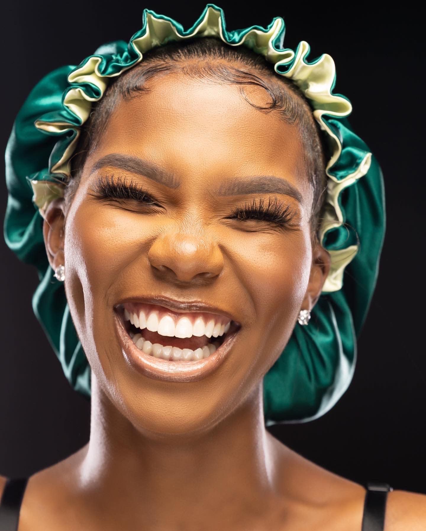 Close up portrait of radiant smile wearing emerald green satin bonnet with ruffled trim.