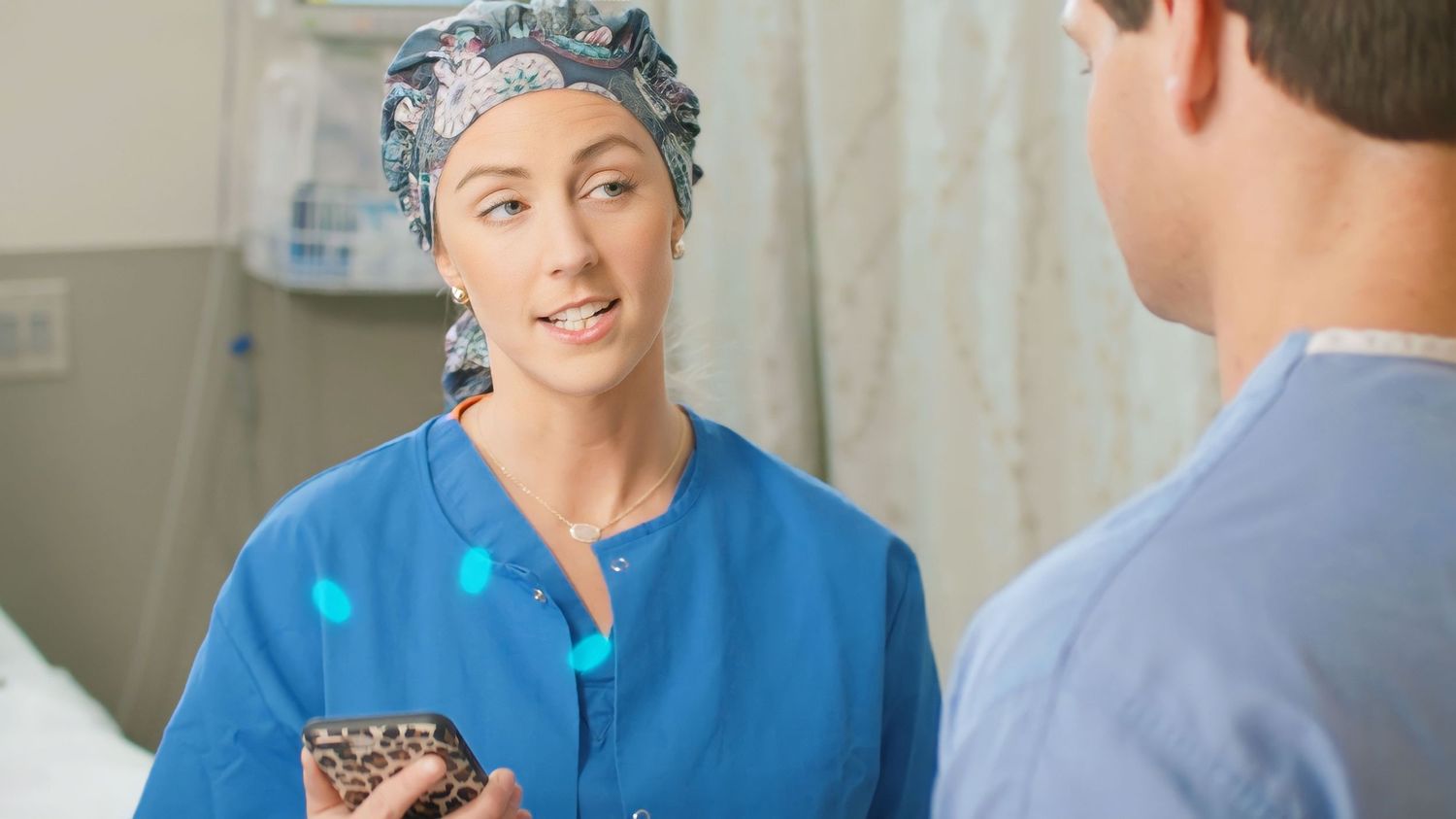 Healthcare professional in blue scrubs holding a portable device in a medical setting.