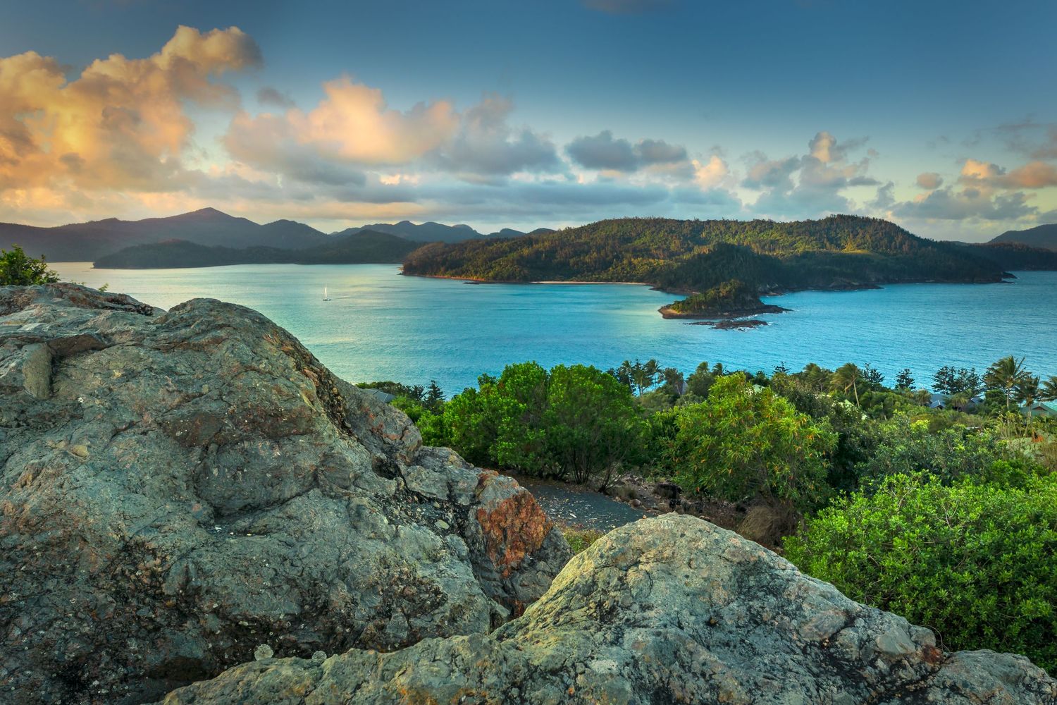 Stunning tropical bay view with turquoise waters and lush islands under golden sunset clouds.