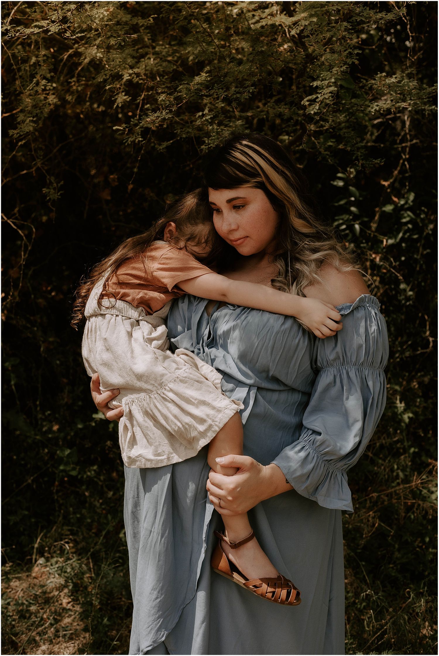 Artistic maternity portrait showing emotional connection in moody forest setting.