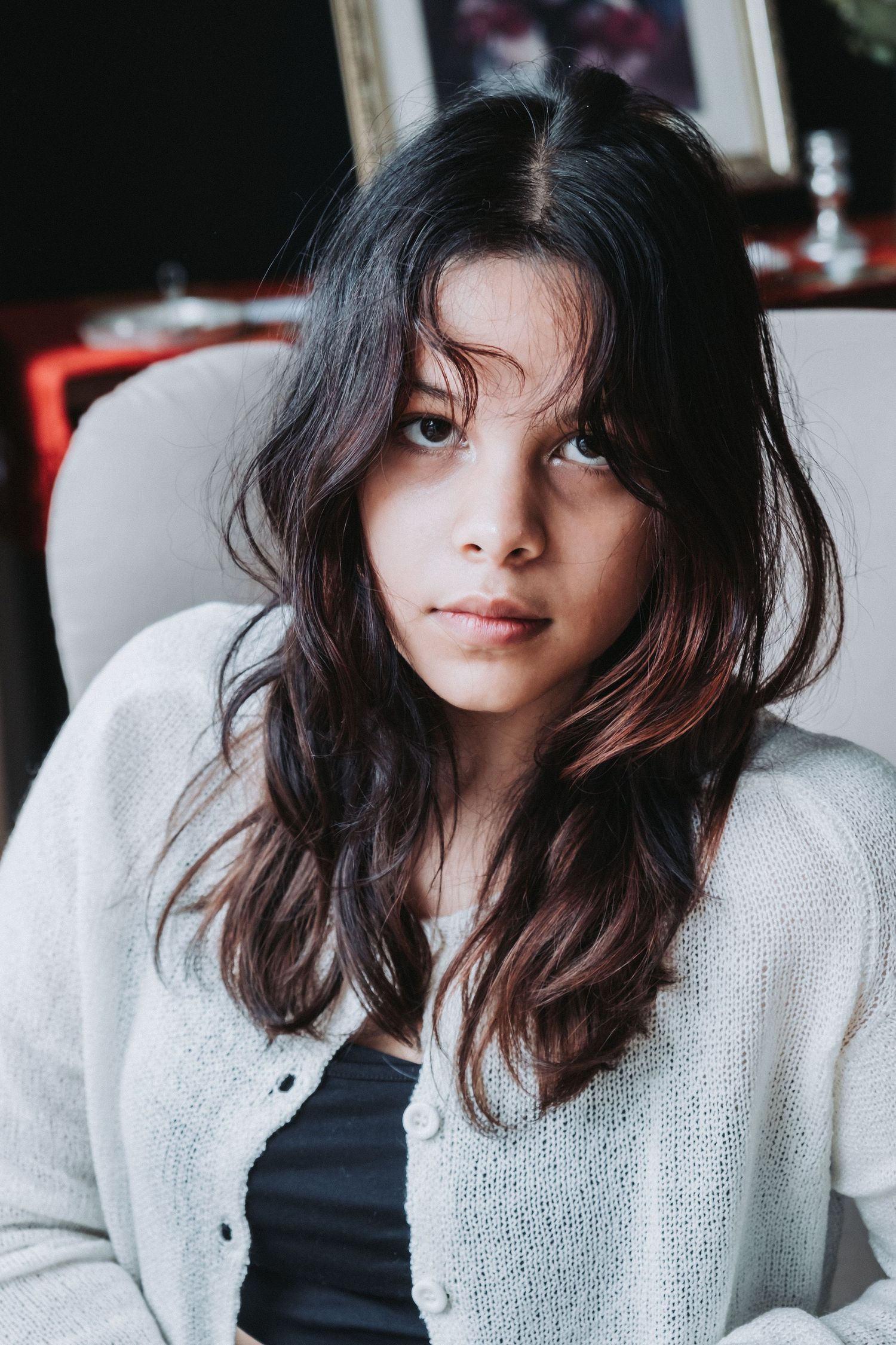 Casual indoor portrait with white sweater and dark hair against moody lighting.