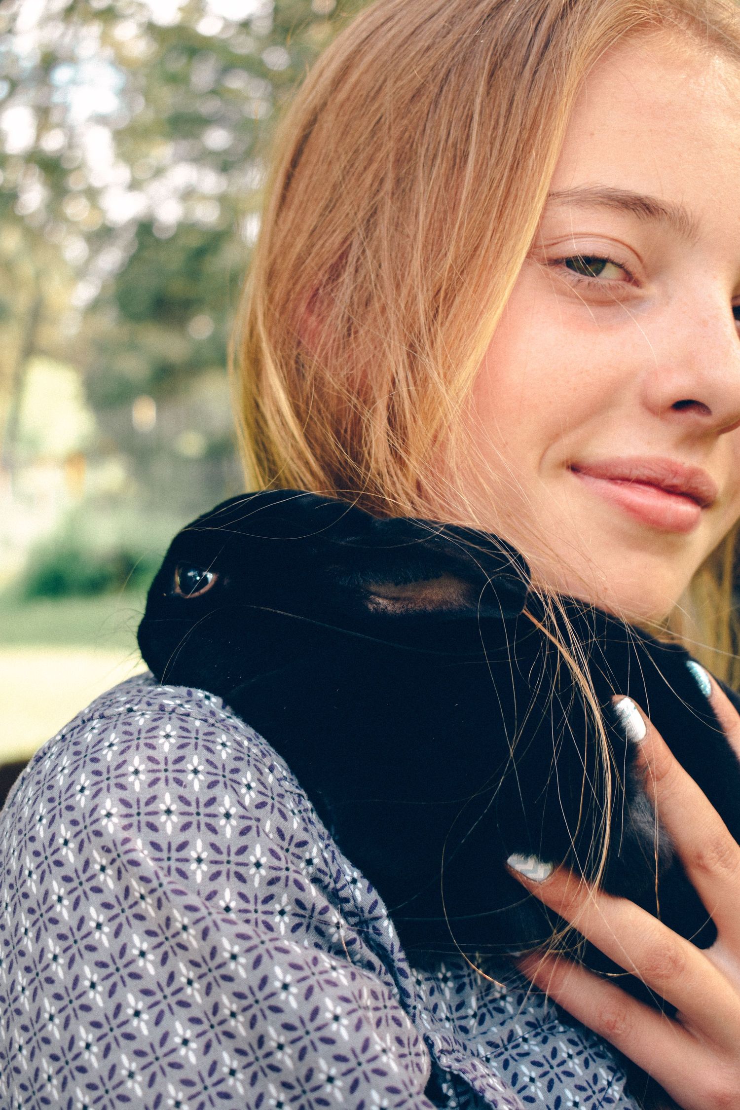 Person in a patterned gray sweater holding a small black rabbit in a natural outdoor setting.