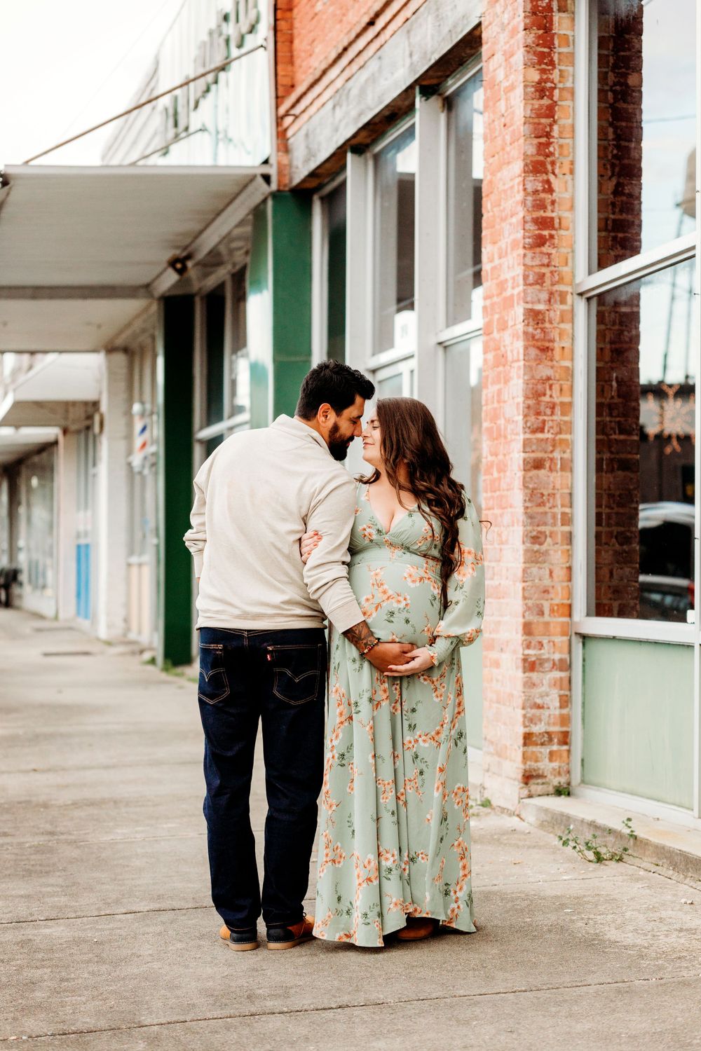 A couple walks together during their maternity session along a vintage storefront.