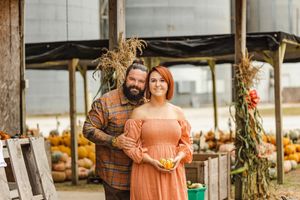 Couple posing together in rustic greenhouse setting with autumn decorations.