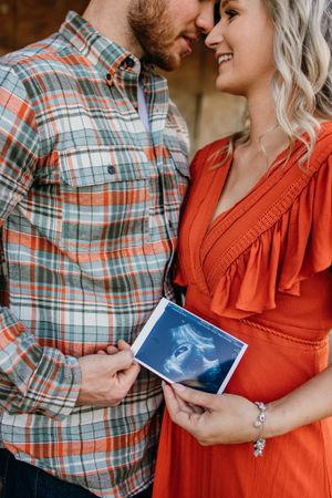 Intimate maternity photos of couple sharing moment while holding ultrasound images.