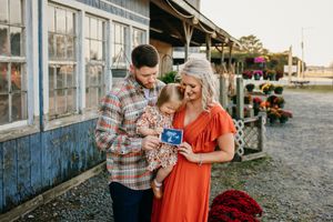 Maternity photoshoot at rustic building with couple looking at ultrasound photos.
