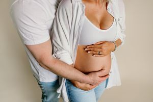 Intimate maternity photo showing couple embracing with hands on pregnant belly in casual white and denim outfits.