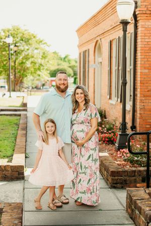 Family posing together outside a red brick building with floral landscaping.