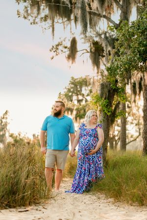 Couple walking along sandy beach path with Spanish moss draped trees.