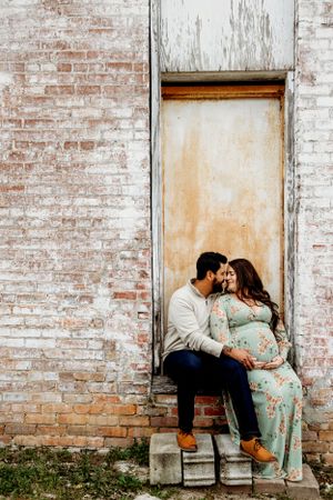 A romantic maternity session against a weathered white brick wall with vintage doors.