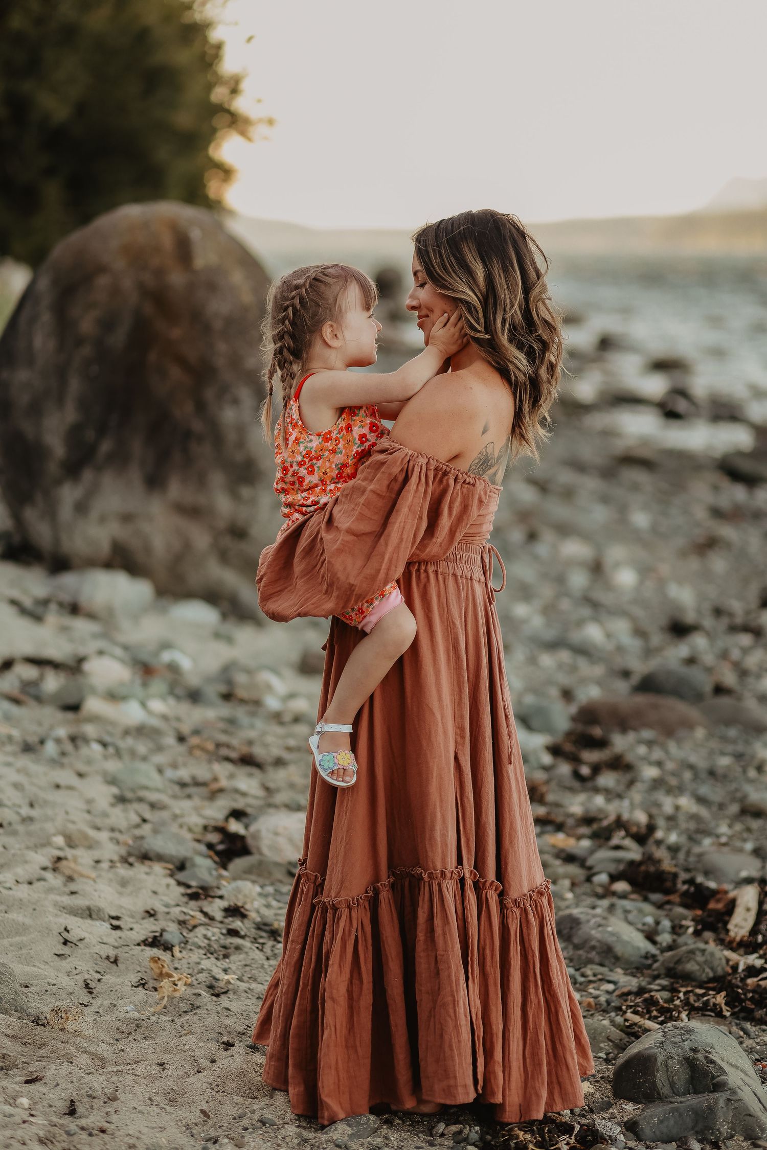 Two rust-colored dresses twirling on rocky beach at sunset.