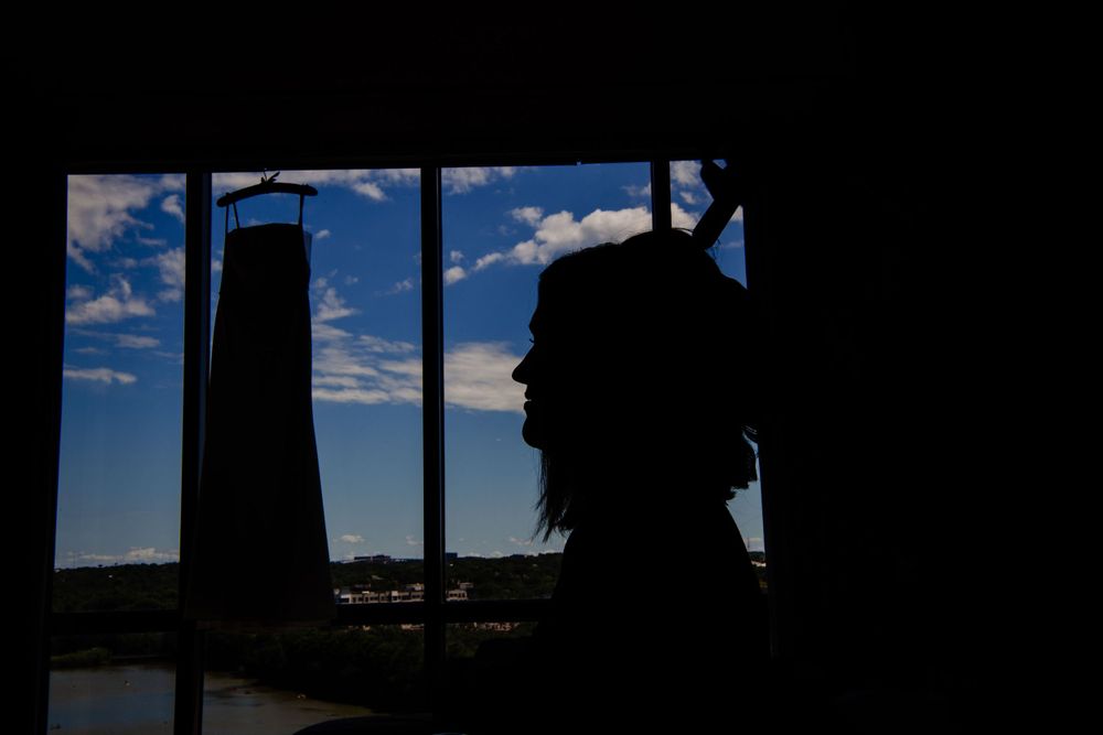 A silhouetted figure gazes out a window with a lighthouse tower visible against a blue sky.