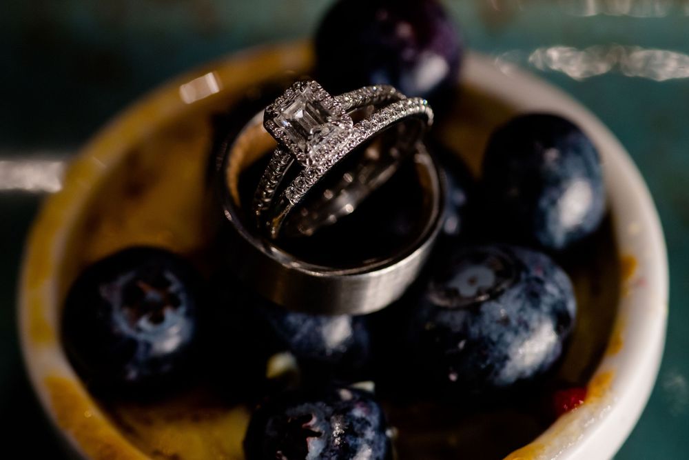 An elegant engagement ring nestled among fresh blueberries on a plate.