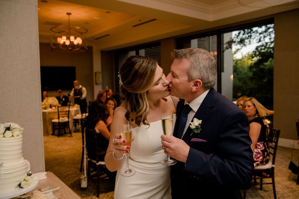 A tender moment shared near an elegant white wedding cake at a reception.