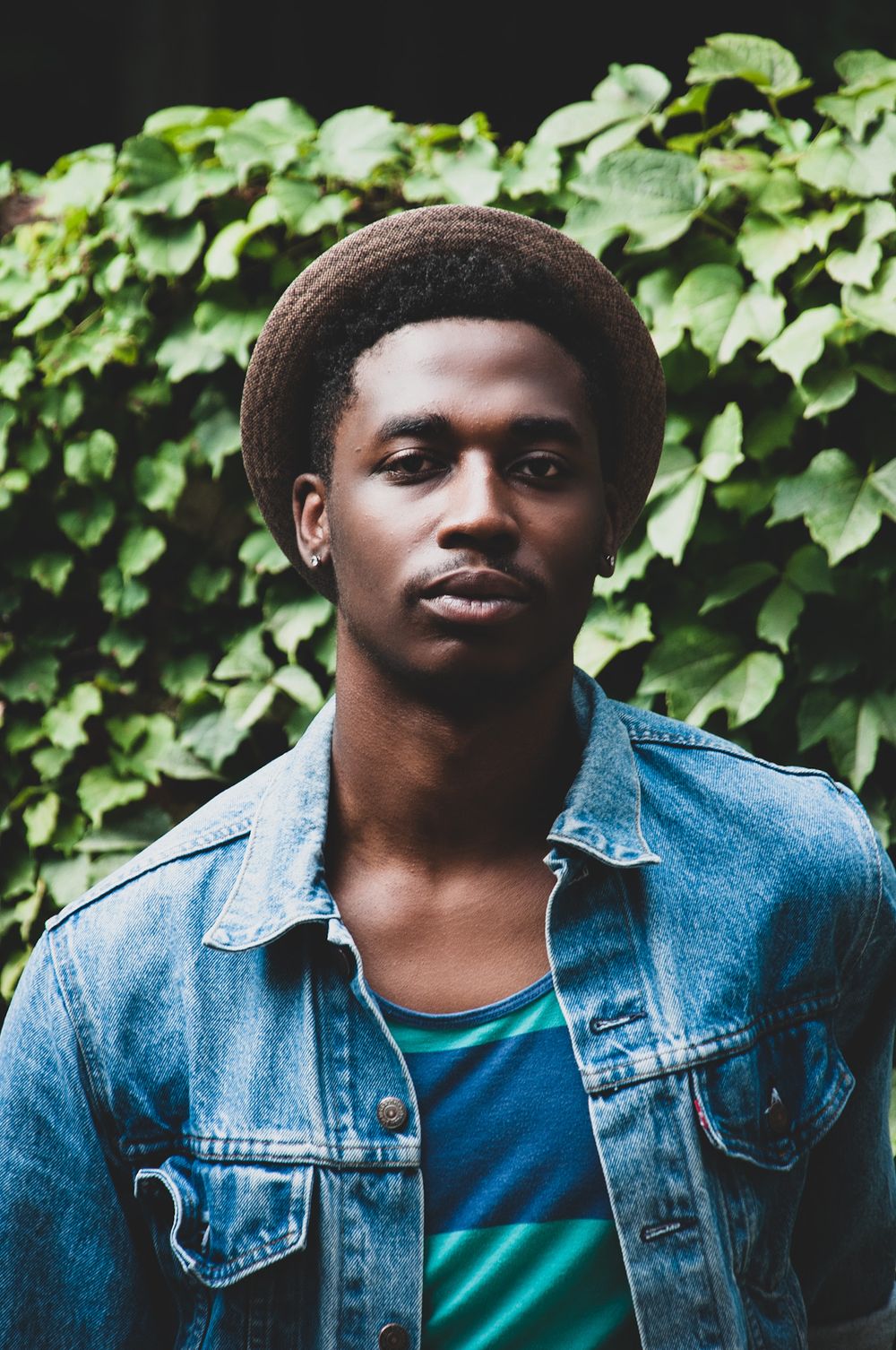 Portrait series of person in denim jacket against ivy wall background.