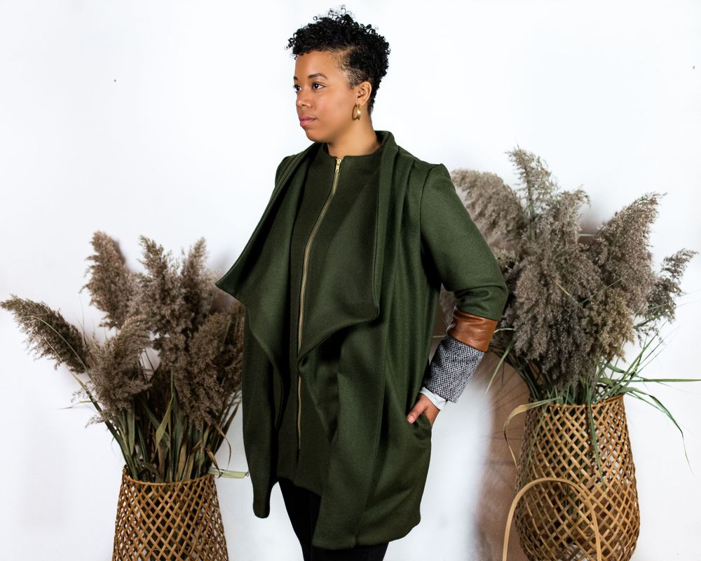 Fashion model in olive green outfit poses with decorative pampas grass and woven basket.
