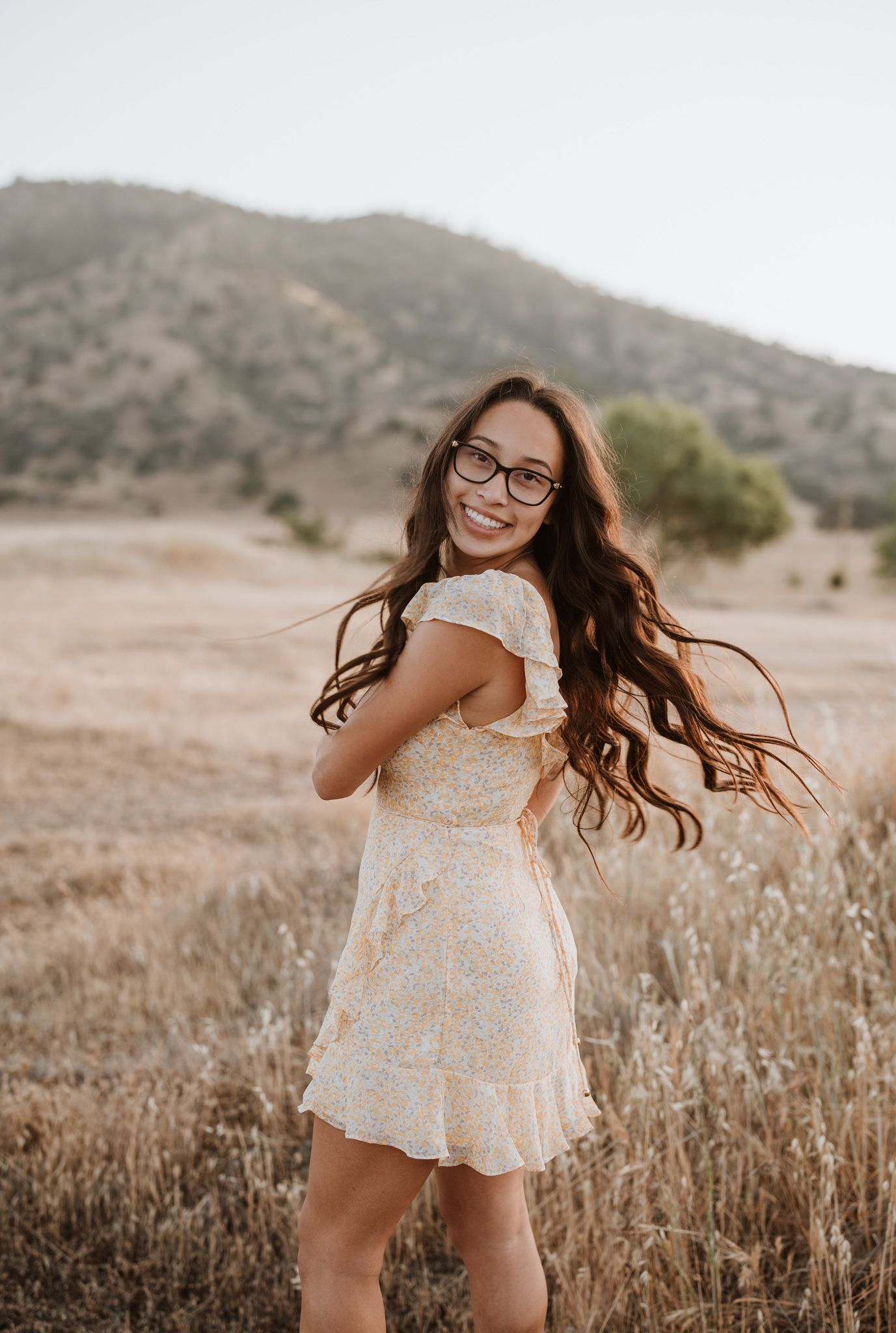 Woman in lace dress spins gracefully in a golden mountain field at sunset.