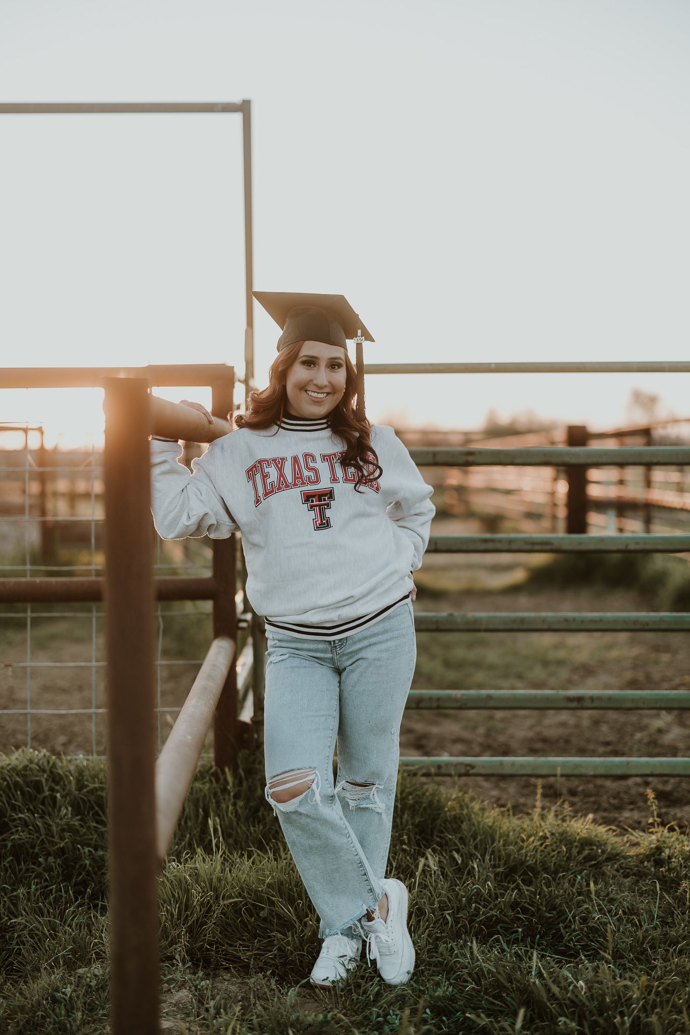 Texas Tech graduate in university sweatshirt poses against rustic fence.