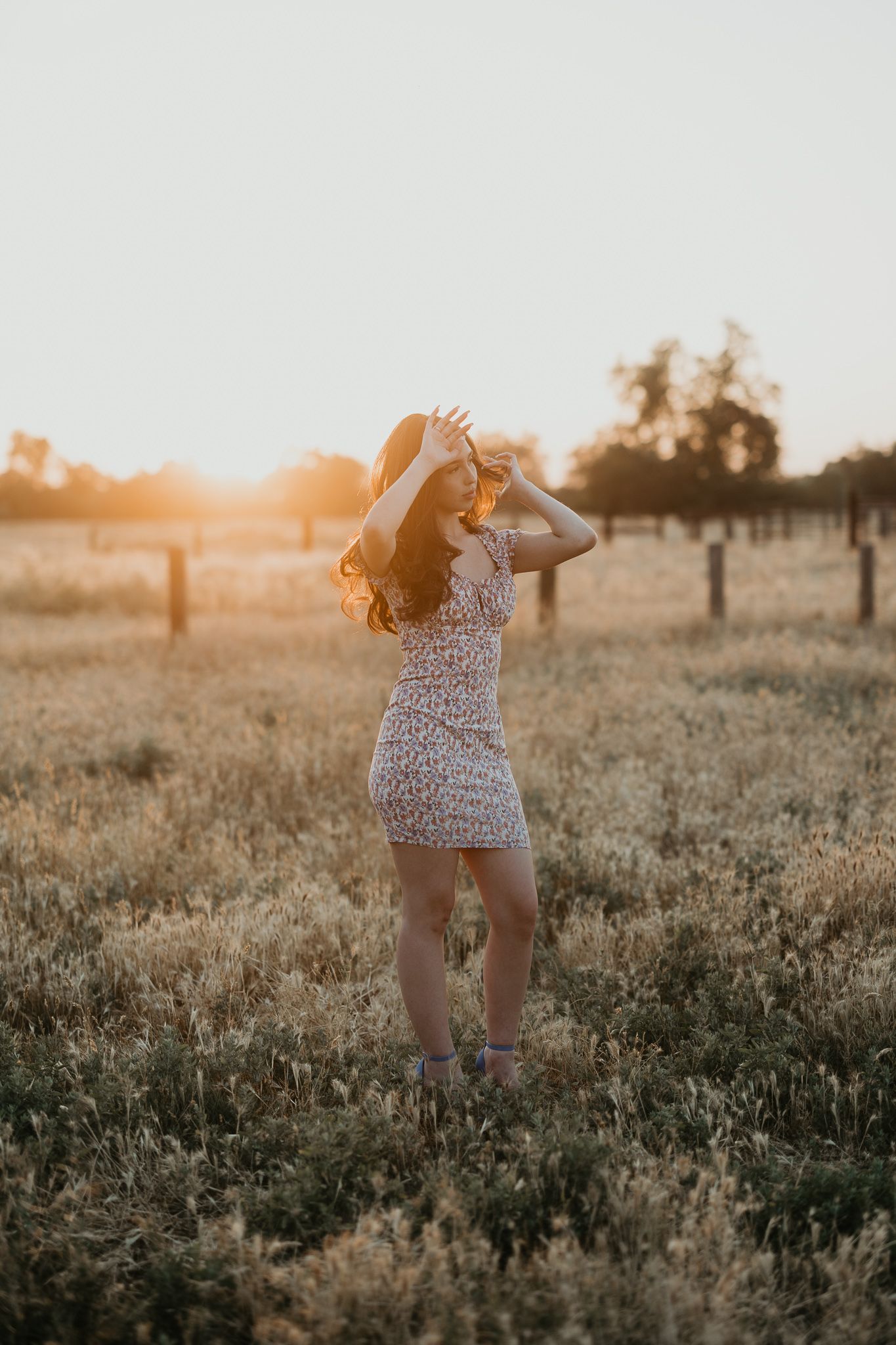 Woman in floral dress posing in field during golden hour sunset.