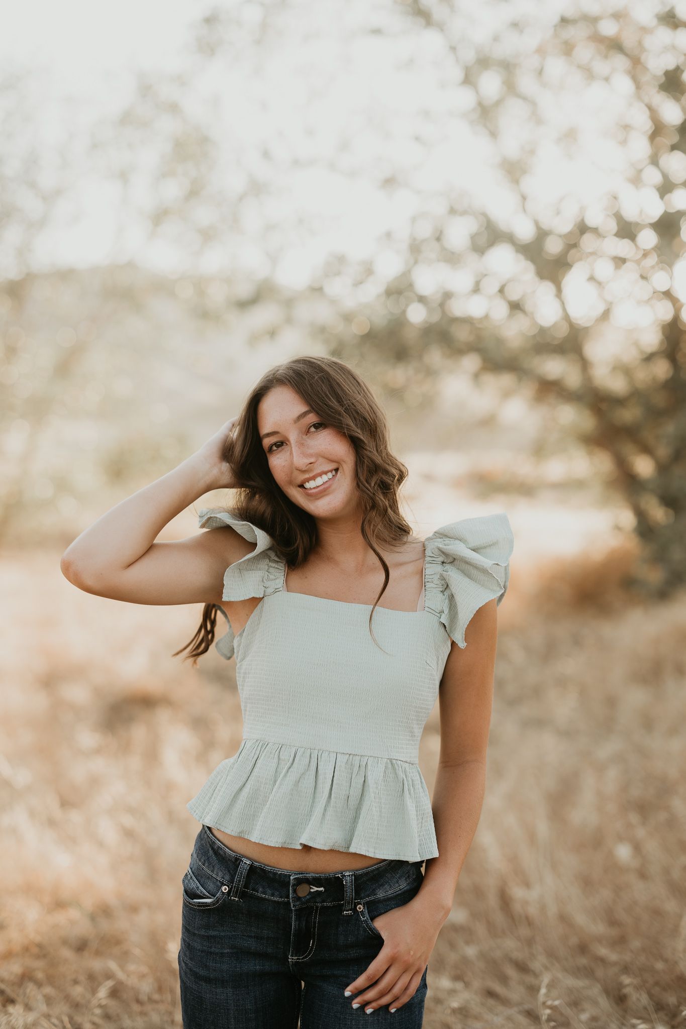 Woman in ruffled crop top poses in golden field at sunset.