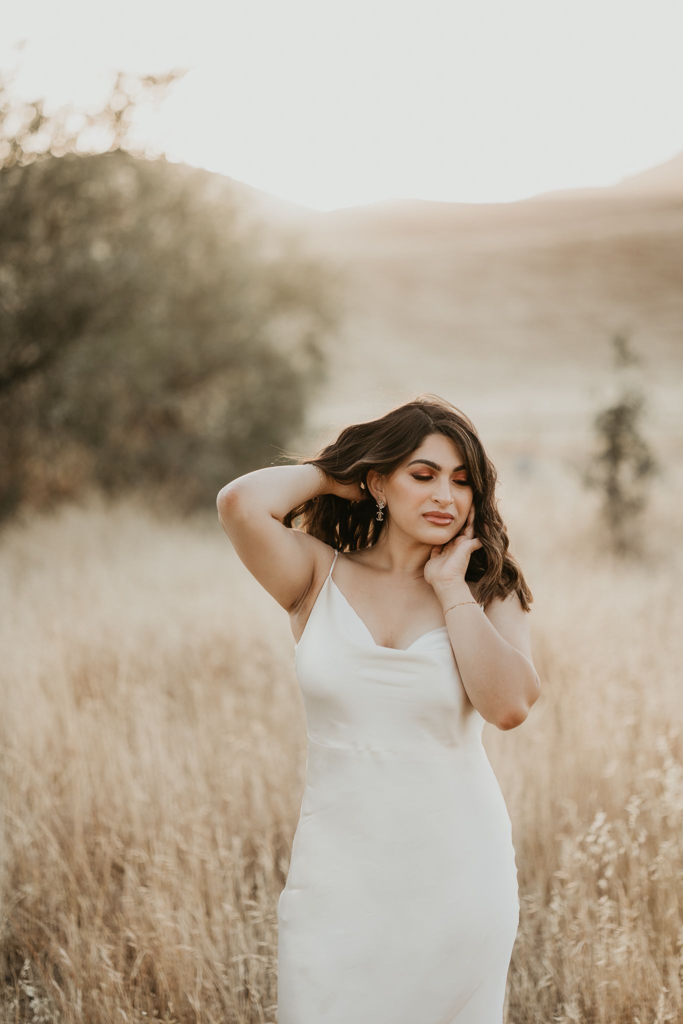 Dreamy outdoor portrait of someone in a white dress surrounded by golden grass at sunset.