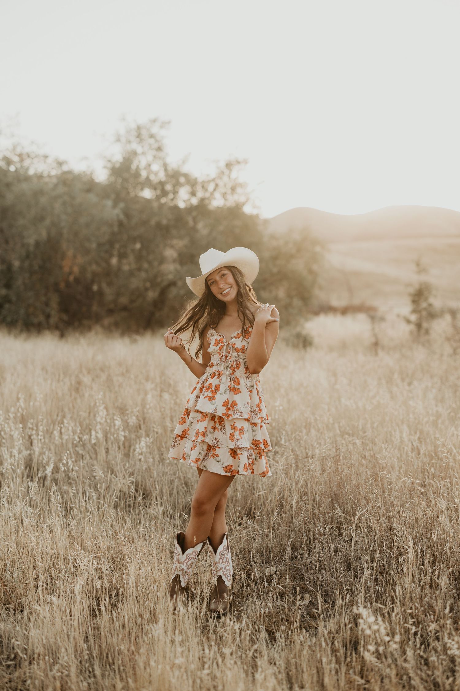 Woman in floral dress and cowboy boots twirls in golden field.
