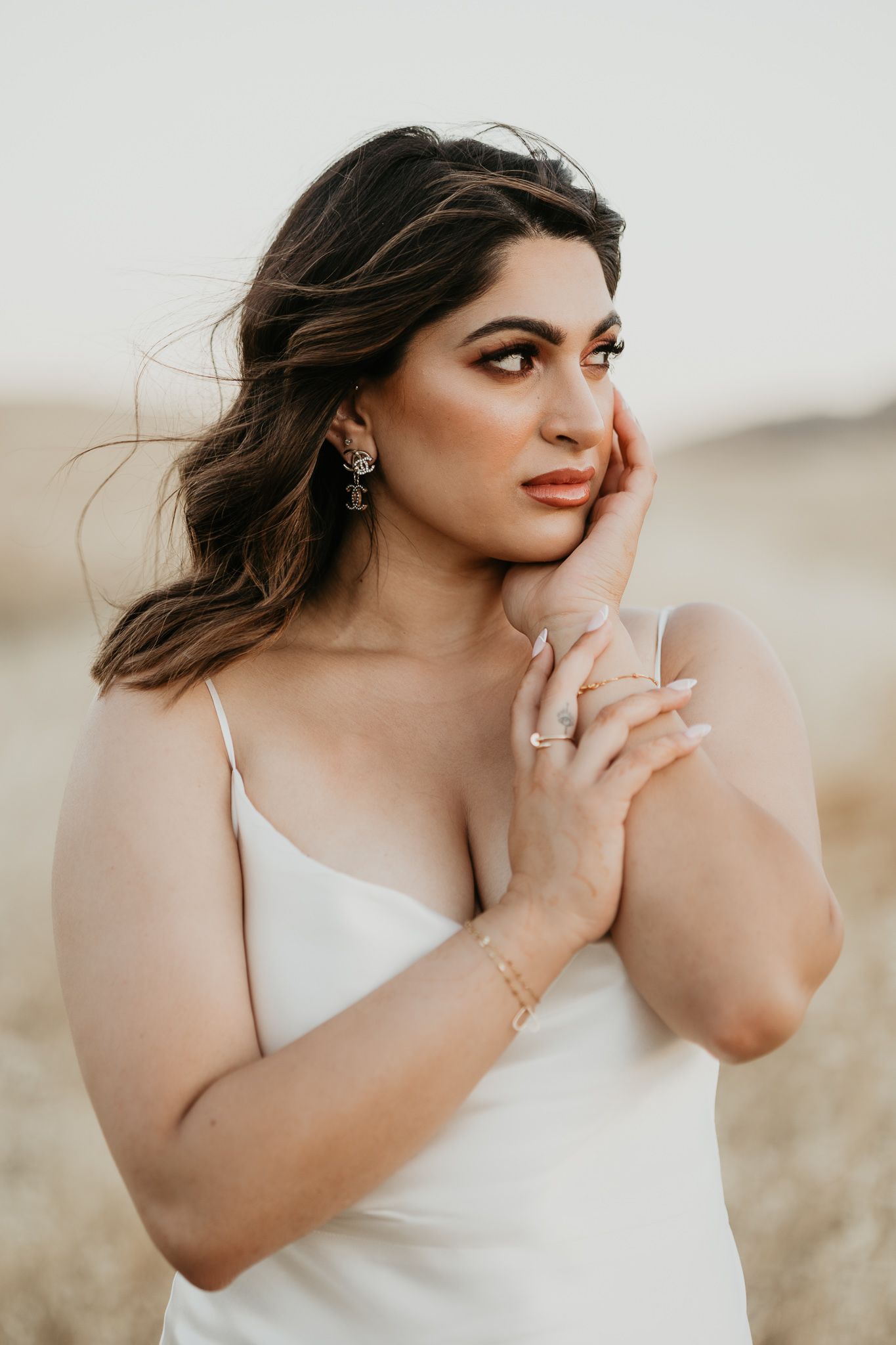 Portrait of a person wearing a white dress and elegant jewelry in a golden-hour outdoor setting.