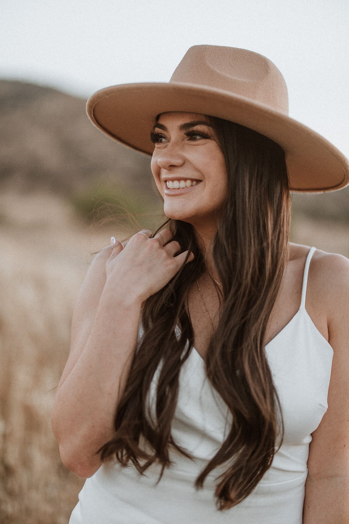Woman in white tank top and tan wide-brim hat posing outdoors during golden hour.