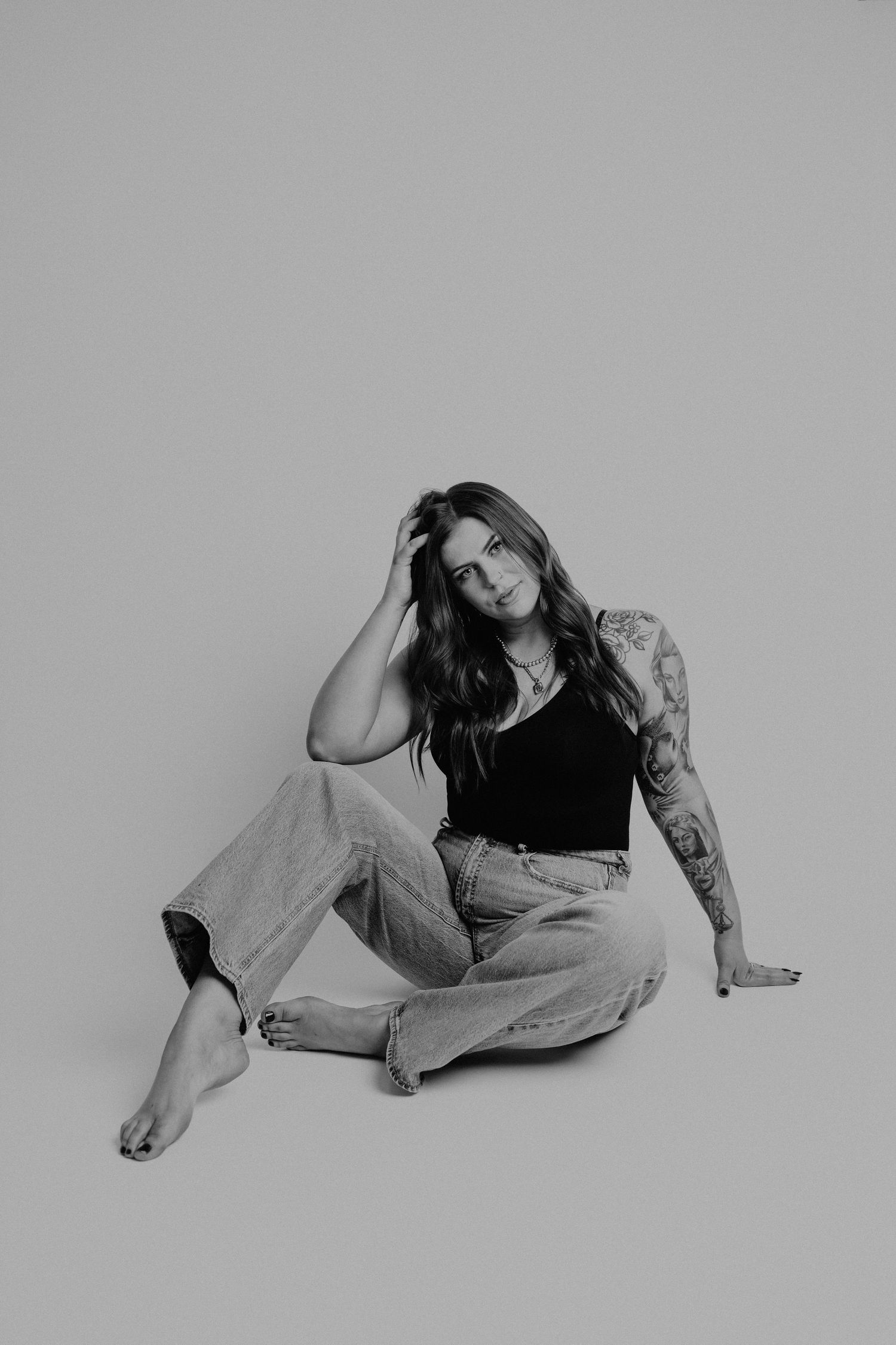 Black and white portrait of a person in casual attire sitting on the floor.