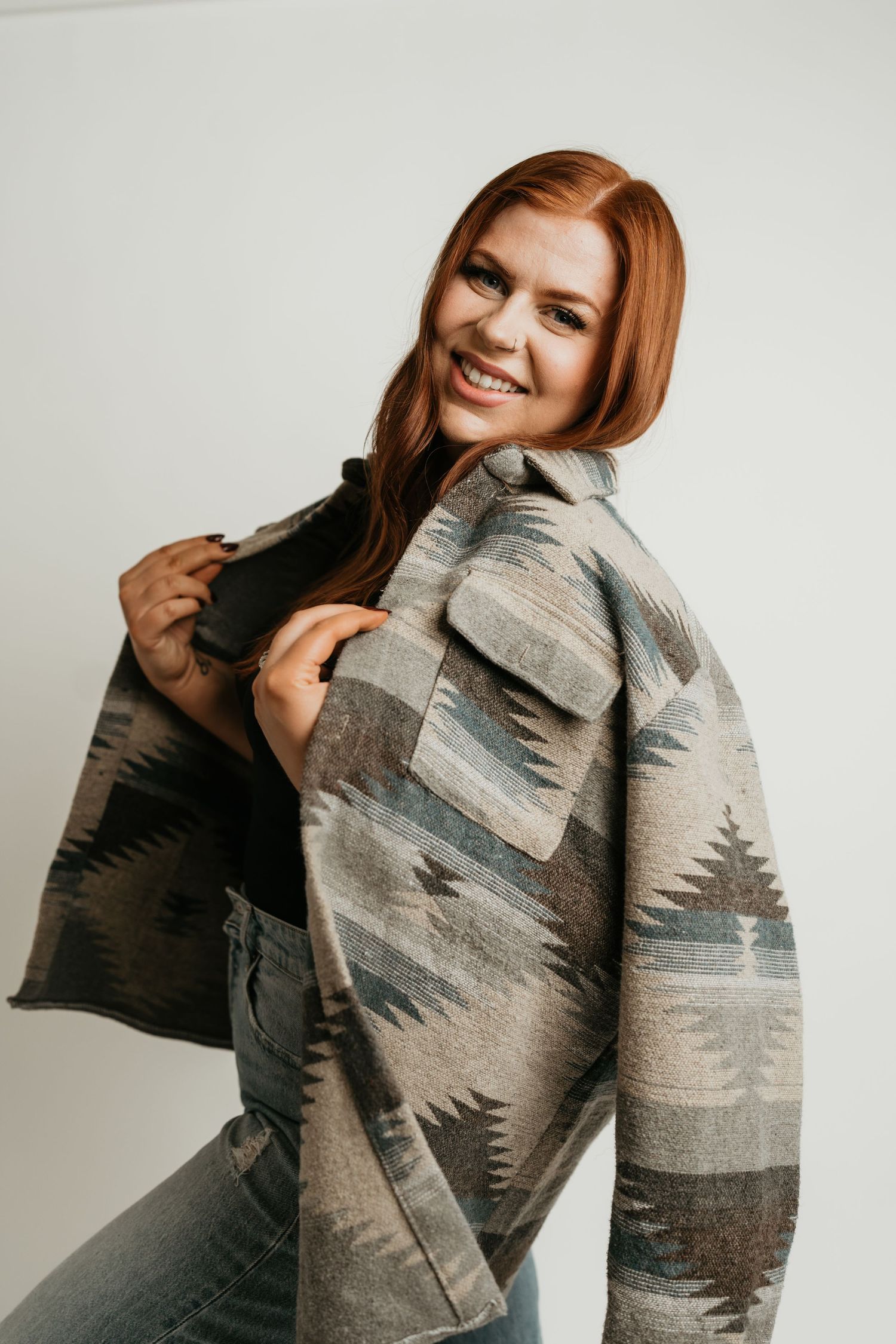 Person wearing a patterned grey jacket smiles while posing against a light background.