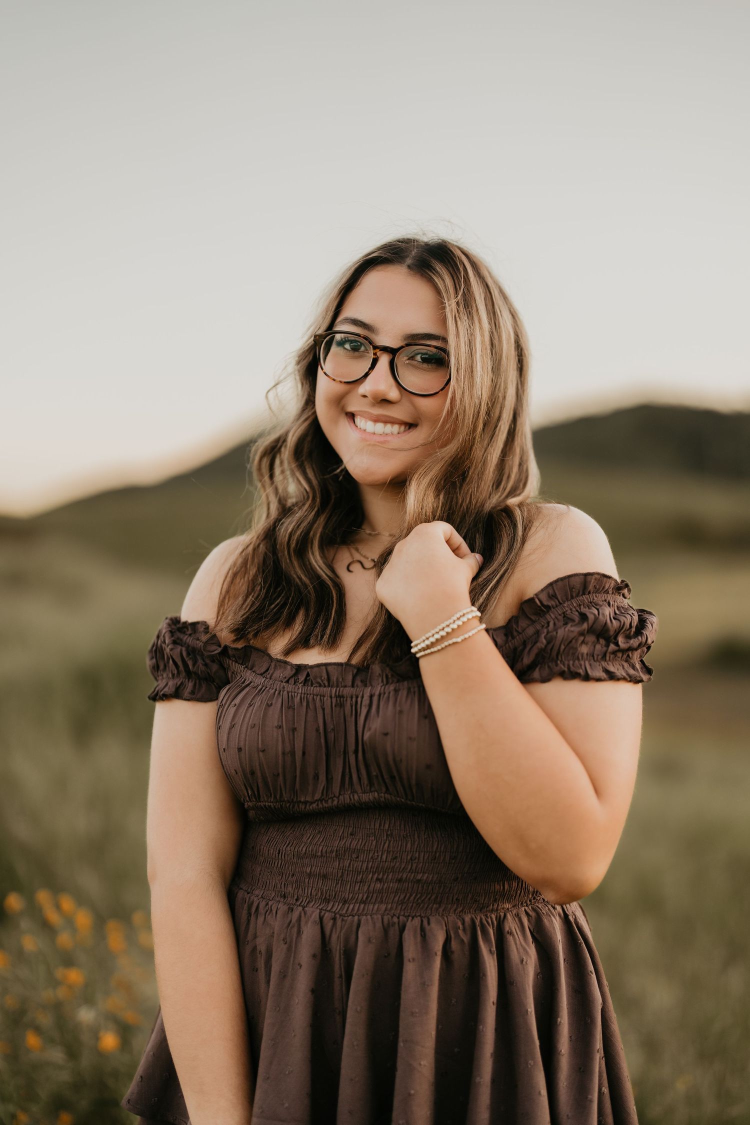 Natural light portrait in a brown dress against rolling hills during golden hour.