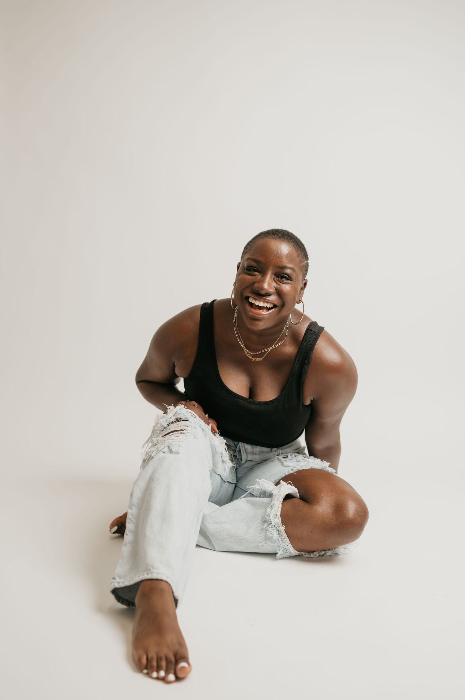 A casual portrait of someone sitting on the floor in distressed jeans against a white backdrop.