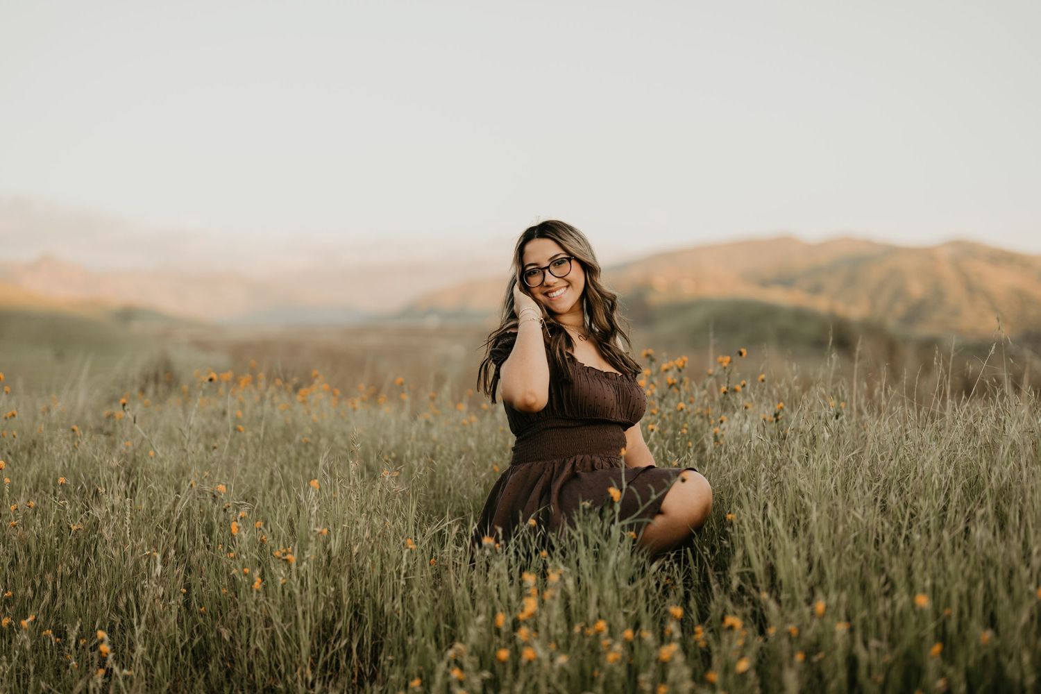 Dreamy outdoor portrait in a field of tall grass with mountains in the background during golden hour.
