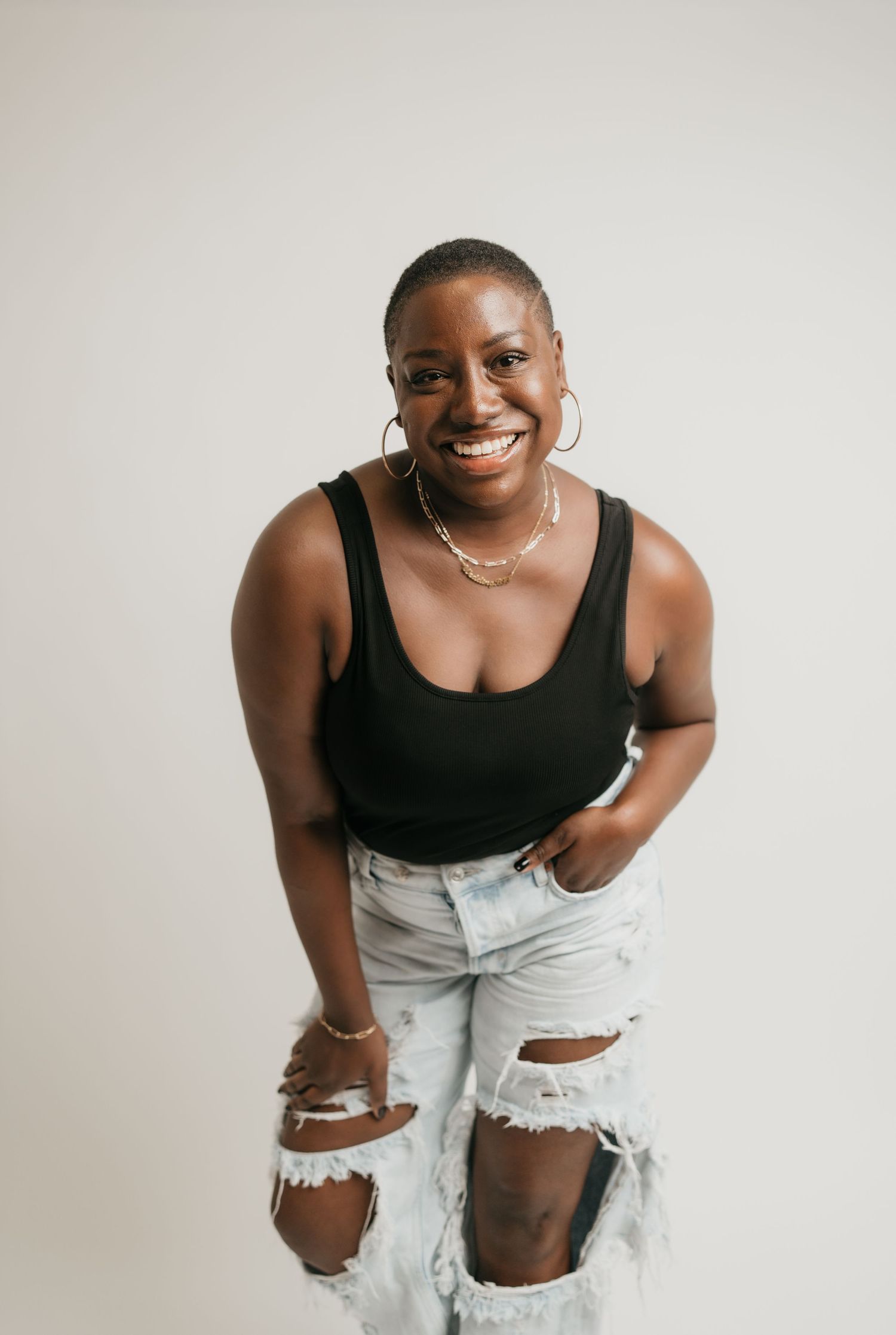 A candid studio portrait of someone wearing ripped jeans and a black tank top.