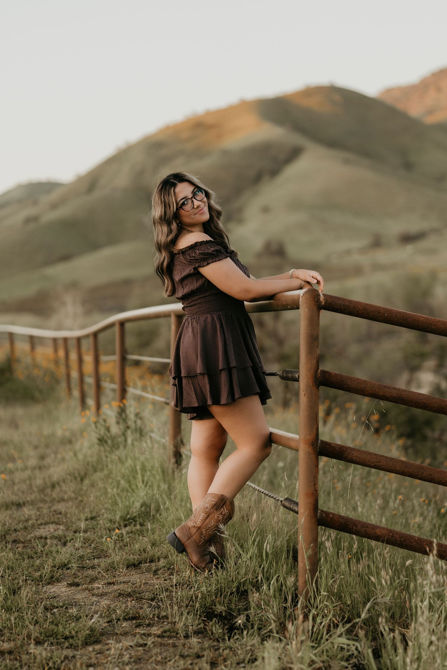 Artistic portrait leaning against wooden fence with scenic mountain landscape at sunset.