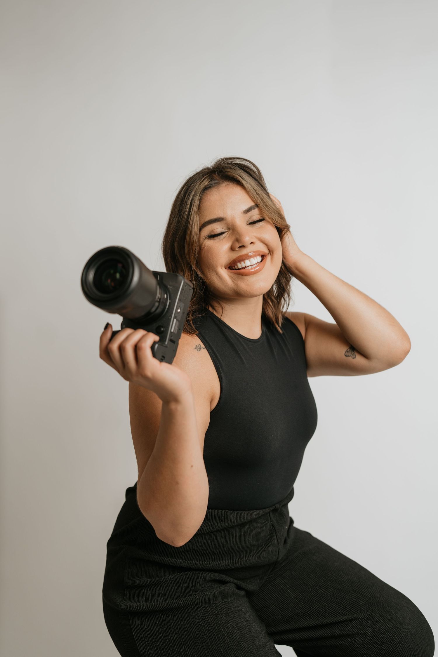 Candid portrait of photographer holding camera while smiling against white background.