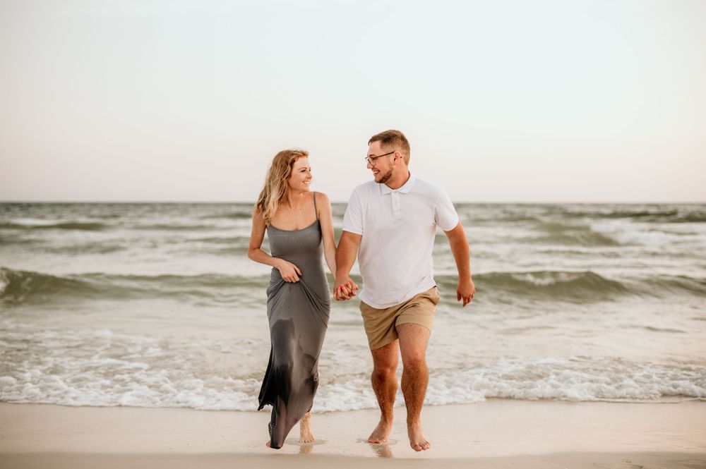 A casual couple walks hand in hand along the shoreline at sunset.
